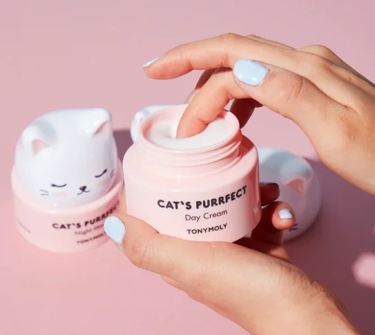Hands opening Tonymoly Cat's Purrfect Day Cream jar on pink background with a cat-themed design.